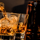 Whiskey in zwei Gläsern mit Eiswürfel fuellen mit Flasche im Hintergrund