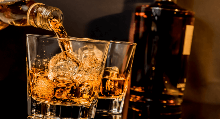 Whiskey in zwei Gläsern mit Eiswürfel fuellen mit Flasche im Hintergrund